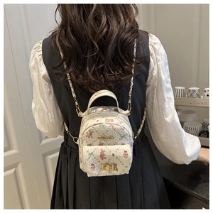 Close-up of white mini backpack with cartoon bear prints and golden metal chain straps