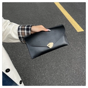 Gros plan d'une pochette enveloppe noire à fermoir feuille dorée tenue à la main avec style