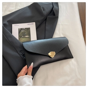 Gros plan sur la pochette enveloppe en cuir noir avec boucle feuille dorée sur veste