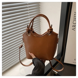 Detail of a brown bucket bag with braided knot handles and DX brand gold embossing