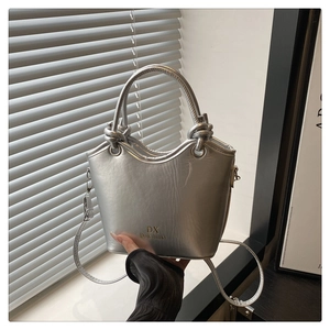 Detail of silver bucket bag with wavy rim, knot handle, and metallic finish surface