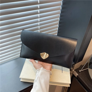 Grande pochette enveloppe noire avec boucle dorée ondulée tenue devant une fenêtre