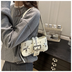 Detail of cream shoulder bag featuring silver rivets, zippers and large metal buckles