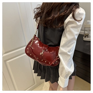 Detail of wine red crescent bag with glossy finish and decorative gold rivets and chain