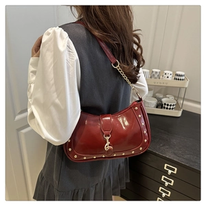 Detail of dark red patent leather crescent bag featuring gold stud trim and chain strap