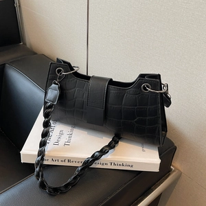 Minimalist black crocodile pattern baguette bag with woven strap on white books