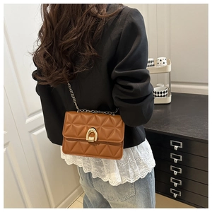 Détail du sac bandoulière marron matelassé avec chaîne dorée sur l'épaule d'un modèle