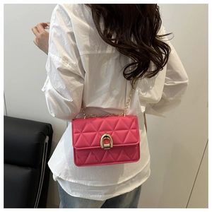 Détail du sac bandoulière matelassé rose rouge avec chaîne dorée sur chemise blanche