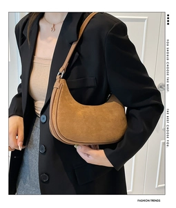 Close-up of brown suede moon bag with silver buckle worn by a model in a black blazer