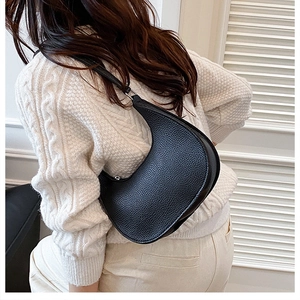 Close-up of black grain leather crescent bag worn by a model in a knit sweater