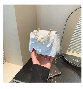 Close-up of white mini girl's bag with pearl handle, bow detail and golden chain strap