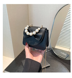 Detail of black pebbled leather crossbody bag with pearl handle and bow accent