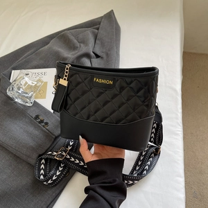 Chic black quilted tote bag with wide patterned strap and golden logo in a stylish setting