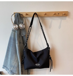 Detail of black nylon crossbody bag with patterned rope strap and metal logo