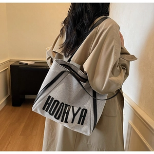 Detail of a large canvas tote bag with leather trim and HOORYA logo on a model