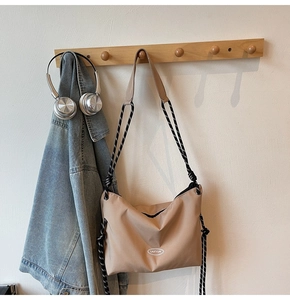 Detail of khaki crossbody bag featuring a woven rope strap and minimalist logo on hook