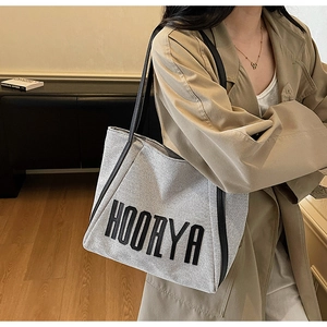 Detail shot of grey canvas tote bag with black leather straps on a model's shoulder