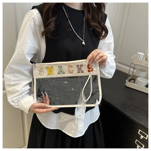 Detail of transparent PVC makeup bag featuring SNACKS chenille patches and cream leather trim