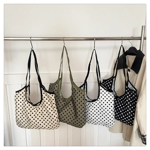 Détail de quatre sacs fourre-tout à pois en beige, olive, blanc et noir suspendus au mur