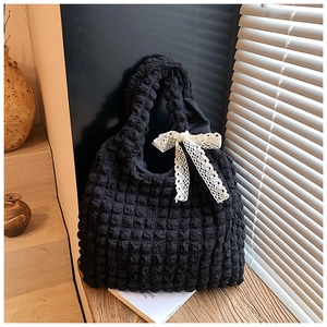 Detail of black puff textured tote bag with creamy lace bow on wooden stairs