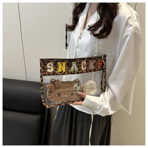 Close-up of clear PVC toiletry bag with leopard trim and colorful SNACKS embroidery detail