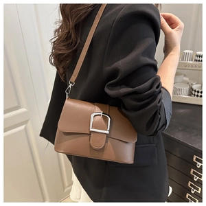 Détail d'un sac bandoulière en cuir marron avec boucle argentée sur un blazer noir