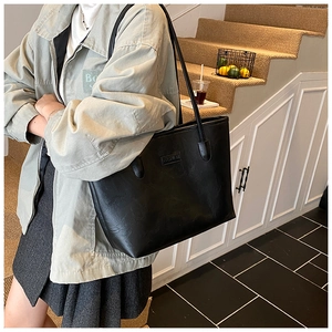 Detail of a black pebbled leather tote bag shown on a model in a minimalist setting