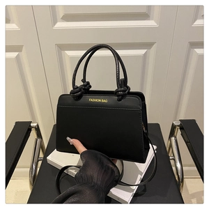 Detail of black rectangular handbag with yellow Fashion Bag text and knotted dual handles