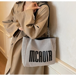 Détail du cabas en toile avec poignée en cuir noir et maillons de chaîne en métal