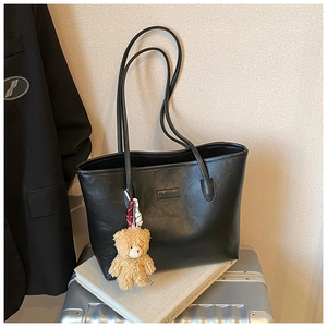 Detail of black faux leather tote bag with FASHION label and brown teddy bear pendant