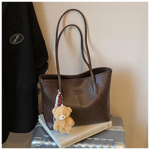 Close-up of deep brown tote bag with fashion patch, plush bear charm and long straps