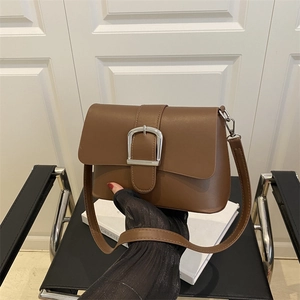 Sac bandoulière vintage marron avec boucle argentée posé sur une chaise et un livre
