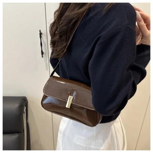Detail of a deep brown patent leather underarm bag featuring a golden buckle on the model
