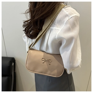 Detail of a beige square shoulder bag with a gold bow buckle and wide woven strap