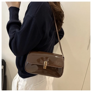 Detail view of a dark brown glossy patent leather shoulder bag with gold metal buckle