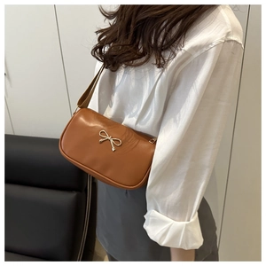 Detail view of a brown leather shoulder bag with a gold bow buckle on a model