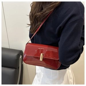 Close-up of shiny red patent leather shoulder bag with a gold rectangular metal buckle