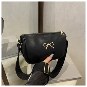 Detail of black matte bag with gold bow clasp and wide fabric strap shown in hand