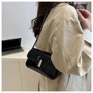 Detail of a black patent leather shoulder bag with sleek metal clasp on a model