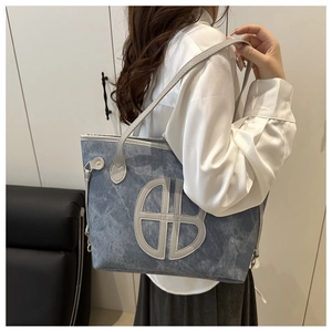 Detail view of denim tote bag with leather logo patch and slim gray shoulder straps