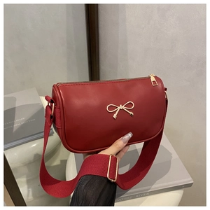 Detail of red cylindrical shoulder bag with gold bow clasp and wide fabric strap