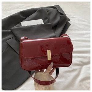 Close-up of burgundy patent leather shoulder bag with a sleek gold rectangular metal buckle