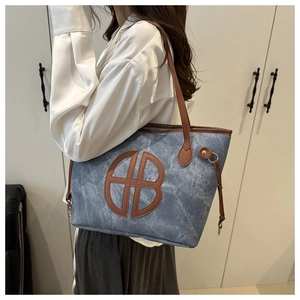 Detail of blue denim tote bag with brown leather straps and embossed HB logo on front