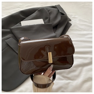 Detail of a deep brown patent leather bag with a glossy finish and gold metal clasp