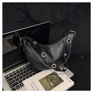 Detail of black crescent hobo bag with silver eyelets and metal chain on a magazine