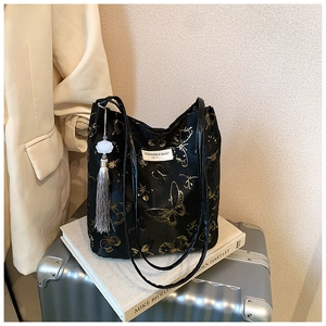 Détail d'un sac cabas noir avec broderie papillon dorée et pompon sur une valise