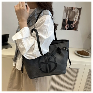 Close-up of dark grey tote bag with embossed B-logo showing matte texture and slim strap