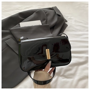 Detailed macro view of the glossy black patent leather finish and gold rectangular metal clasp