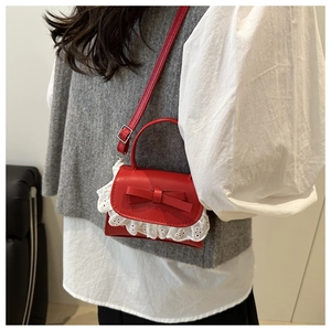 Detail of red mini crossbody bag featuring leather bow and white lace trim edge