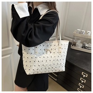 Close-up of white tote bag with black bow embroidery and gold bow pendant detail